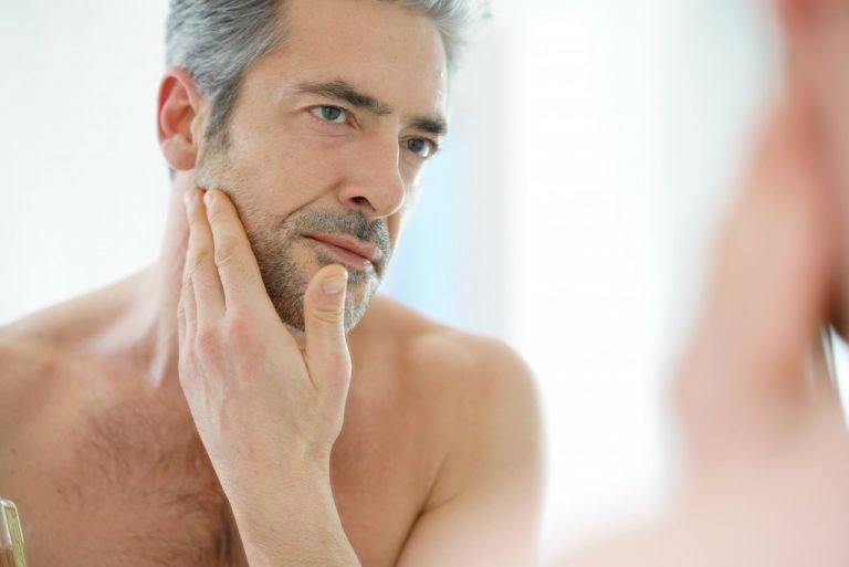 Portrait of mature man in front of mirror applying facial cream