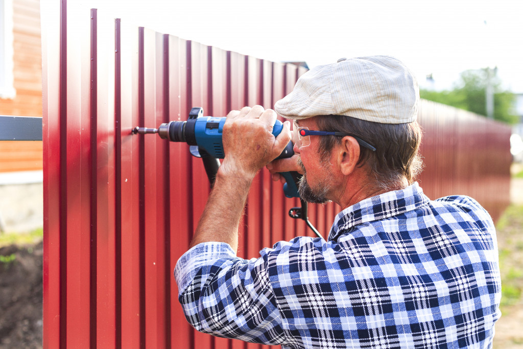 A man wearing eye protection while using a drill to attach a metal sheets on a steel bar to build a fence