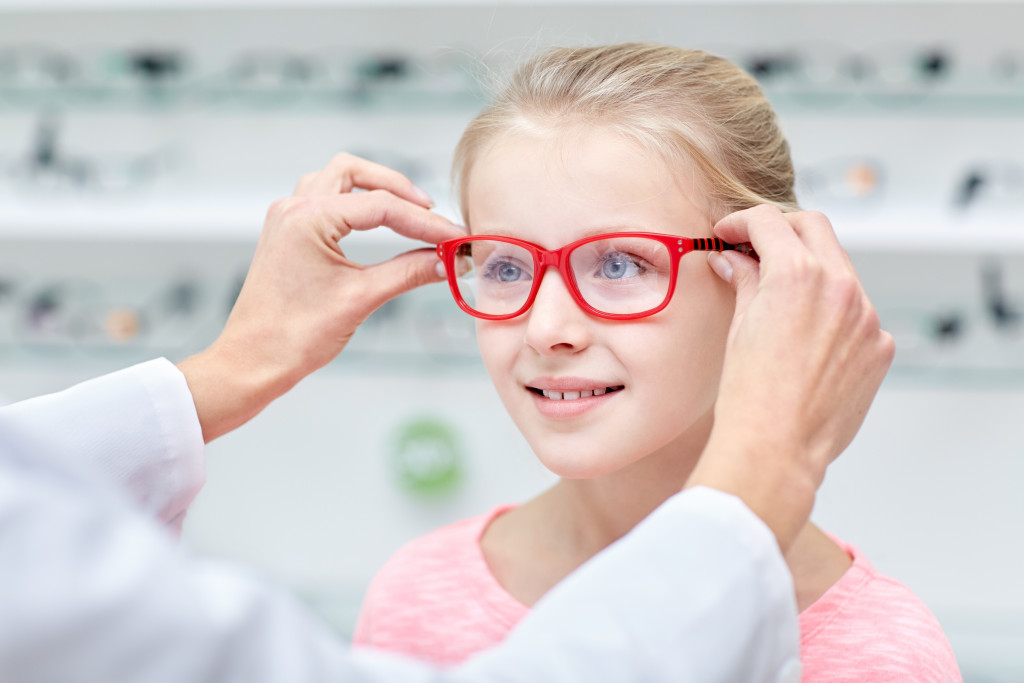 eye doctor putting glasses on young girl in store