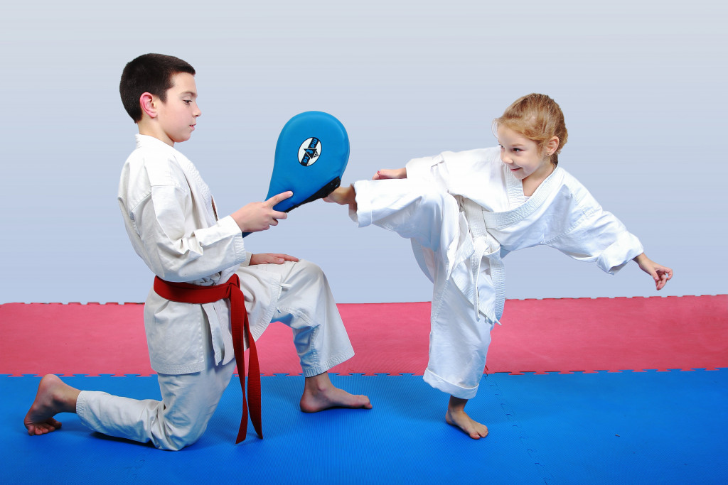 A white belt little girl kicking a simulator held by a boy with red belt