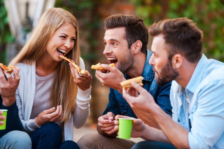 Young people bonding while eating pizza outdoors