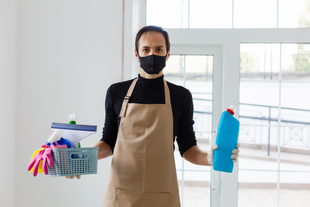 A man holding cleaning items while wearing a mask