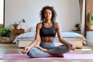curly haired woman meditating in a yoga mat wearing activewear in bedroom