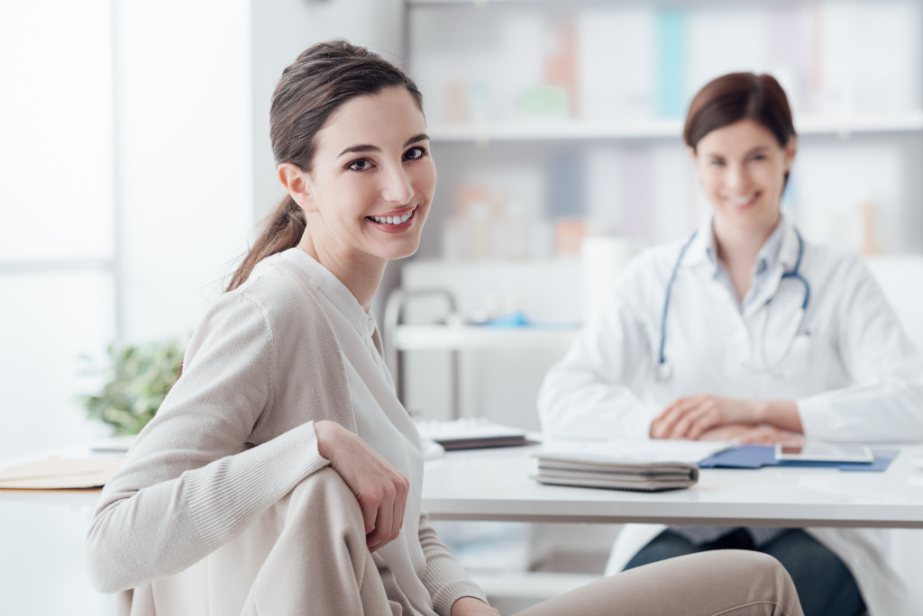 Young woman smiling with a female doctor behind her inside a clinic