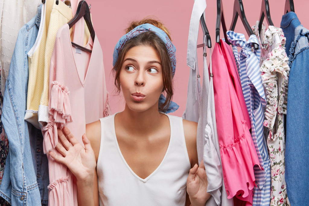 woman choosing from a rack of clothes with pink background