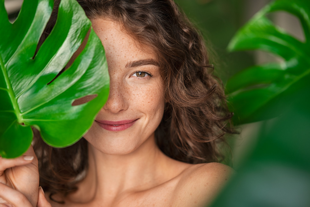 beautiful woman smiling behind big leaves representing natural beauty